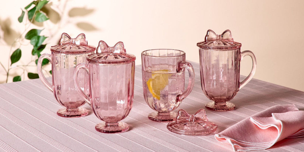Think Pink collection pink glass goblets with lids and bow handles on a striped pink tablecloth, one with a lemon slice.