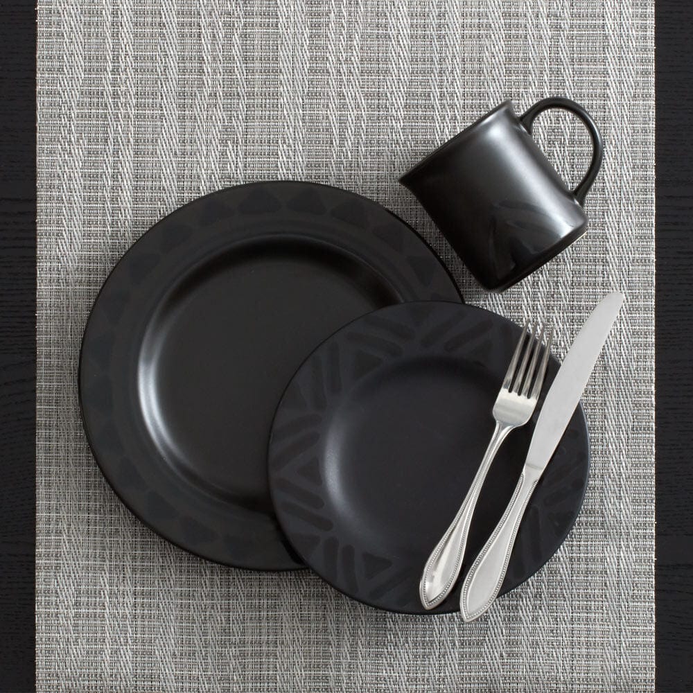 Top-down view of a black matte mug beside two dark plates and silverware on a textured placemat.