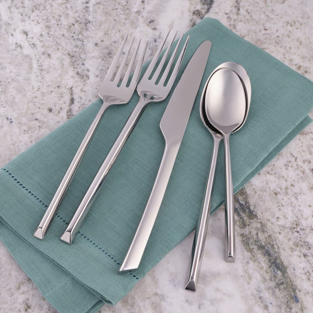 Jacqueline Forged 20 piece flatware set for four with forks knives and spoons arranged on a teal napkin
