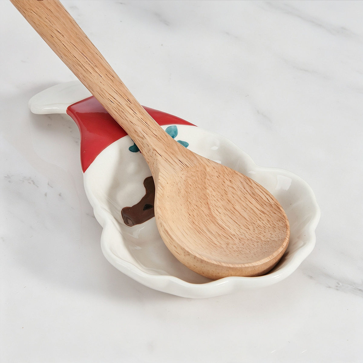 Wooden spoon resting on a Winterberry Jolly Santa spoon rest with white and red ceramic and blue floral accent.