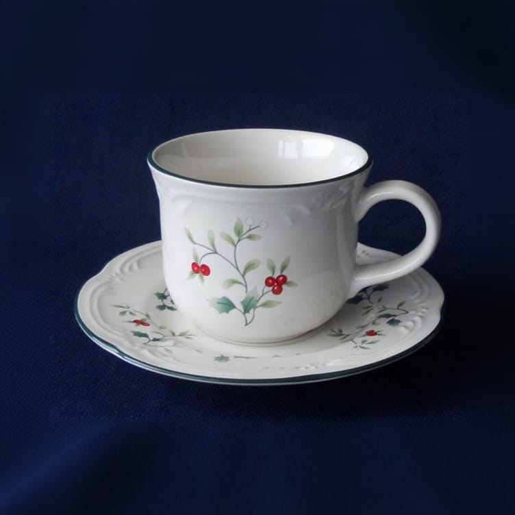 Winterberry cup on matching saucer with holly motif against a dark blue background.