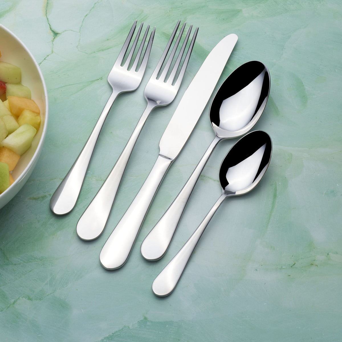Stainless steel forks knives and spoons arranged diagonally from a 20 piece flatware set for four