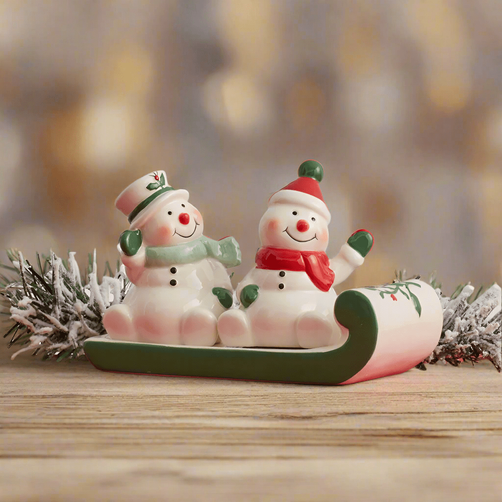 Winterberry snowmen on sled salt and pepper set displayed on a wooden surface with frosted pine greenery in the background