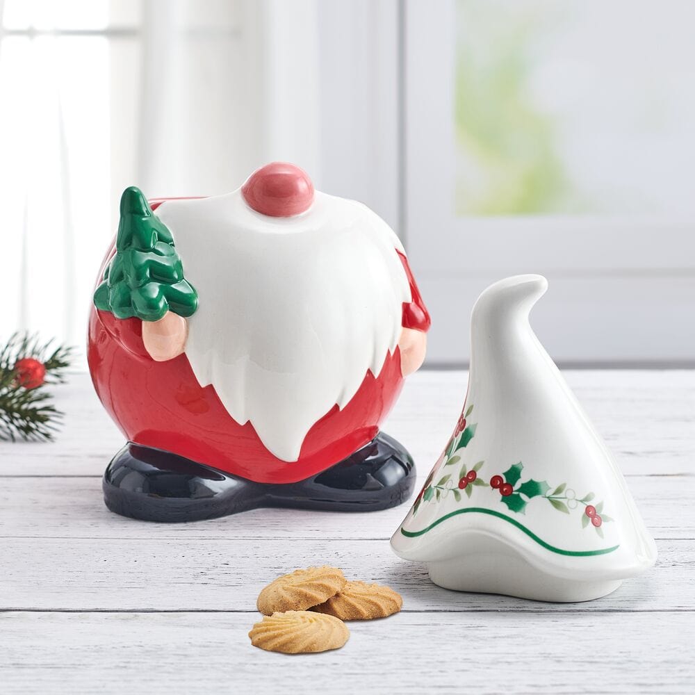Winterberry Gnome Cookie Jar featuring a red body white beard pink nose and black base with a holly decorated lid nearby.