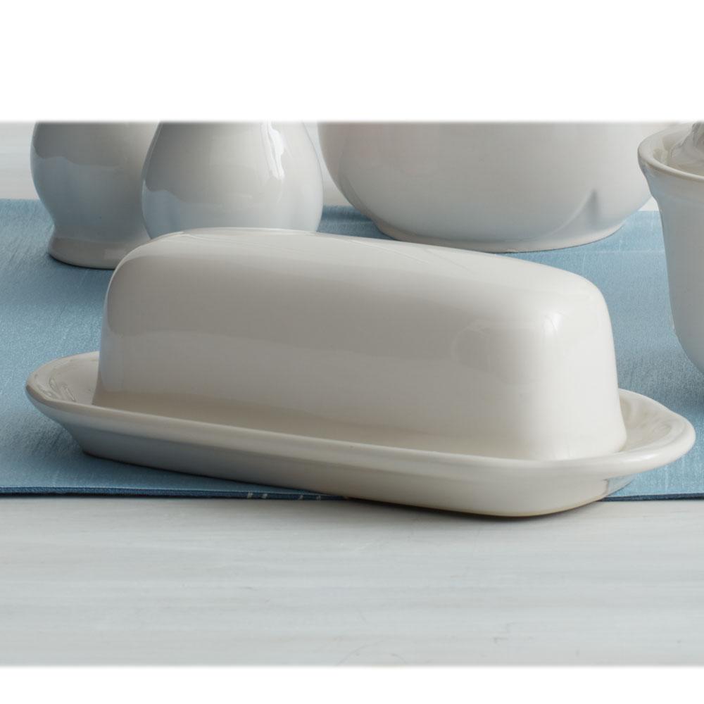 White ceramic covered butter dish on an oval base with a blue placemat underneath
