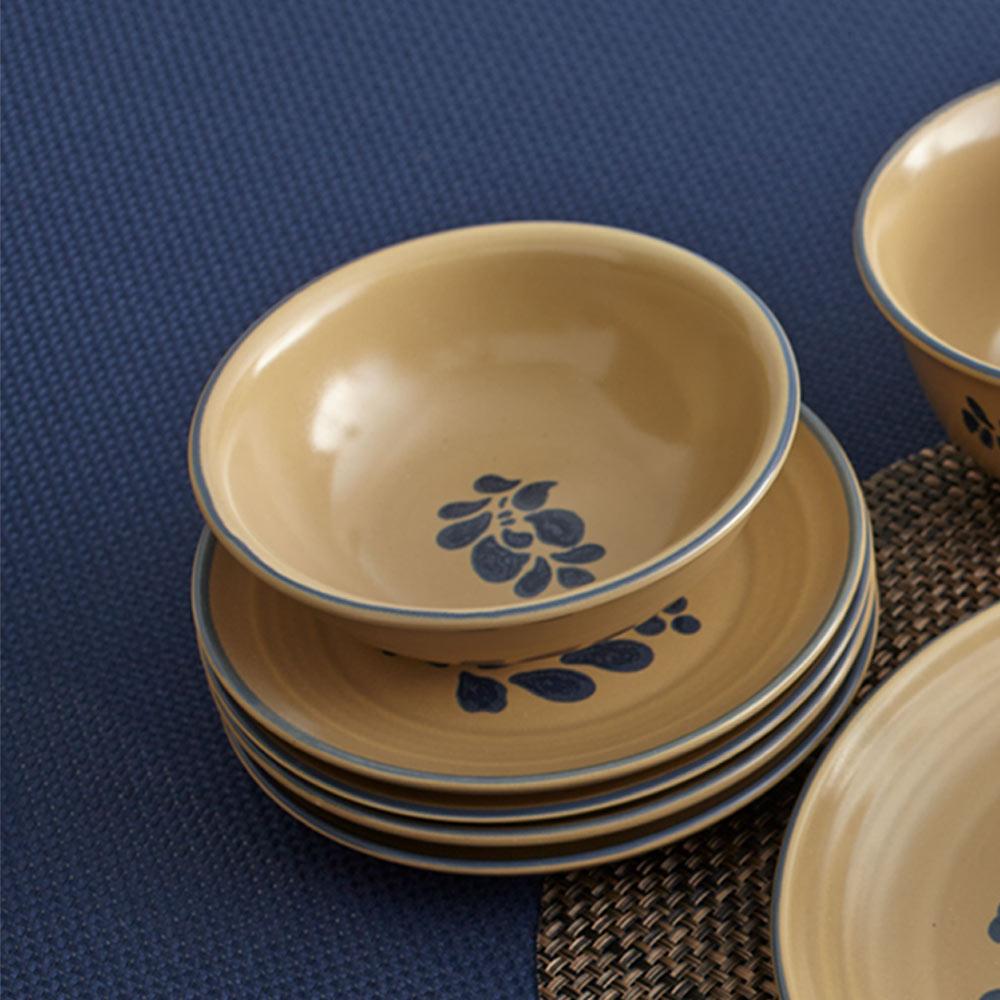 Folk Art set of four beige bowls with blue floral pattern, stacked on a blue surface