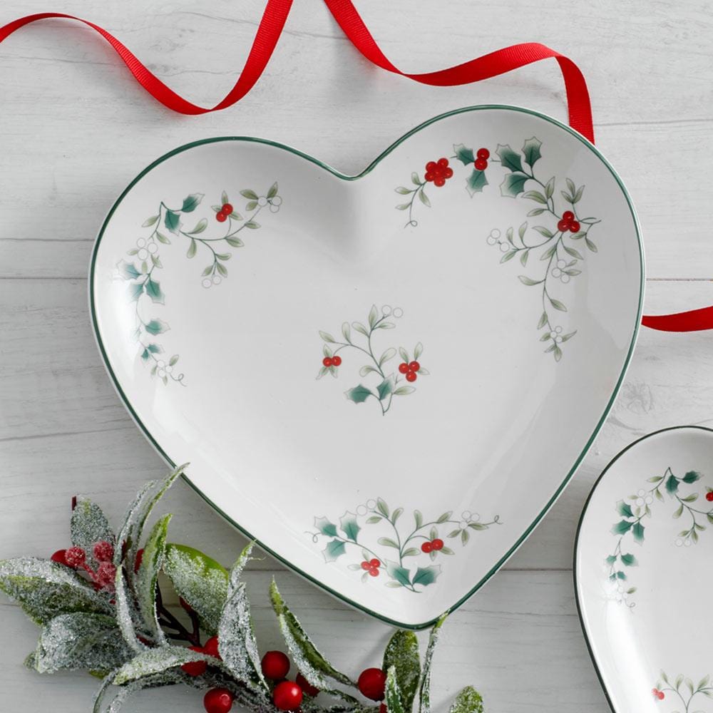 Heart shaped Winterberry platter with holly and berries pattern and green rim, shown with a red ribbon.