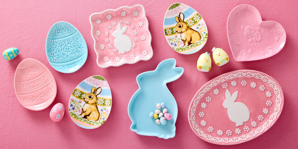 Pastel Easter ceramic set with bunny silhouettes decorative eggs and floral motifs on a pink backdrop.