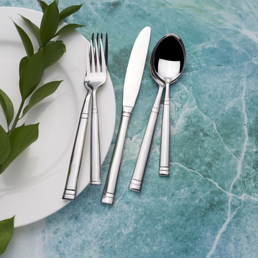 Stephanie forged 20-piece flatware for 4 arranged on a white plate with green leaves on a turquoise marble surface.