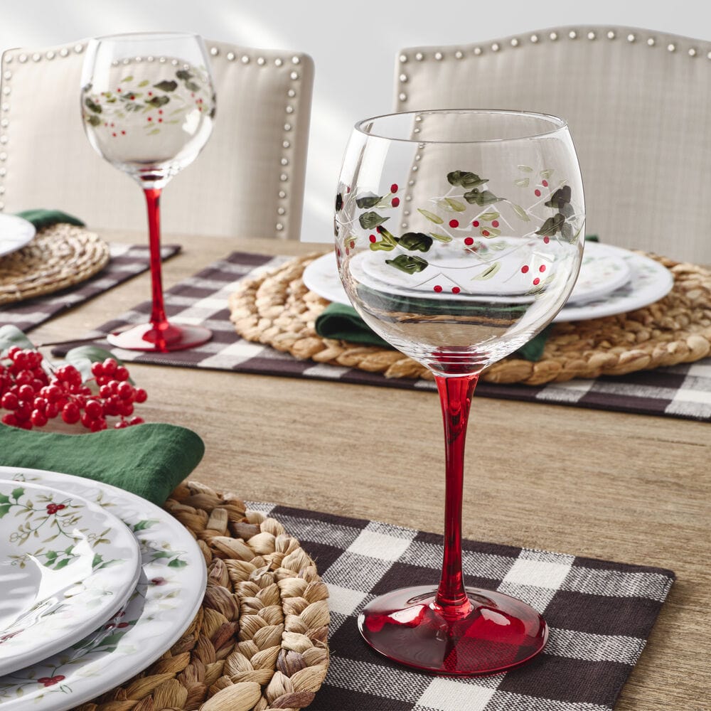 Set of four Winterberry hand painted wine goblets with red stems on a festive table setting.