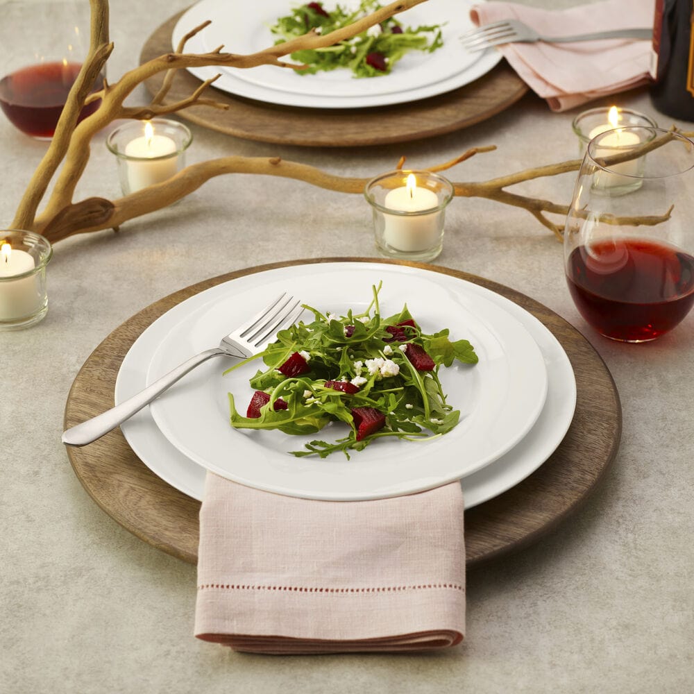 Table setting with a natural mango wood charger plate under a white plate with salad and candles