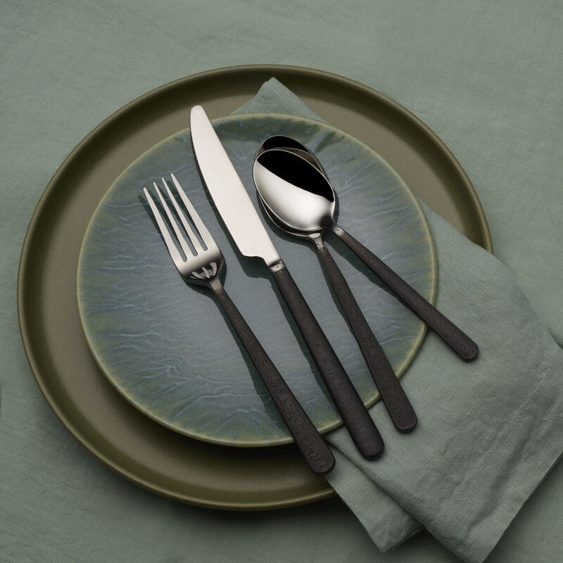 Calyx Black Forged 20 piece flatware set for four displayed on a green plate with a napkin