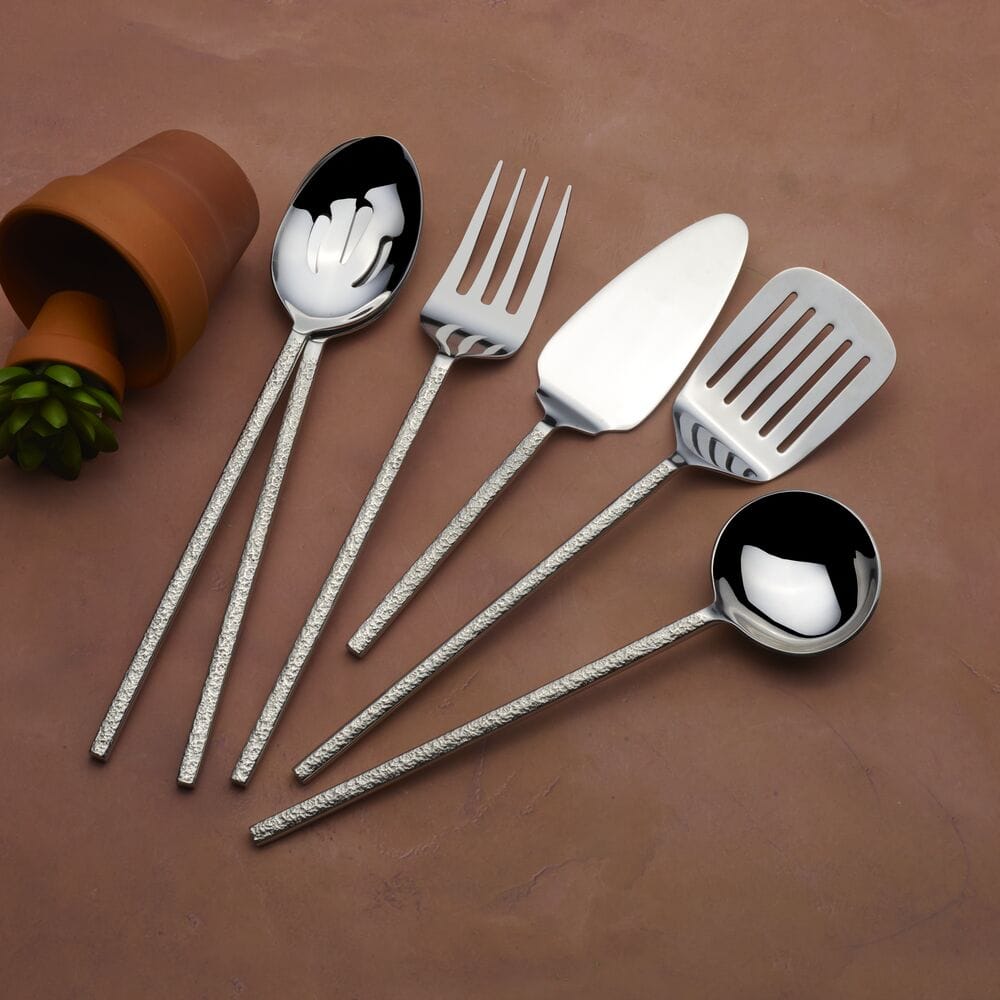 Paragon Forged 6 piece serving set with textured handles arranged on a brown surface beside a small plant