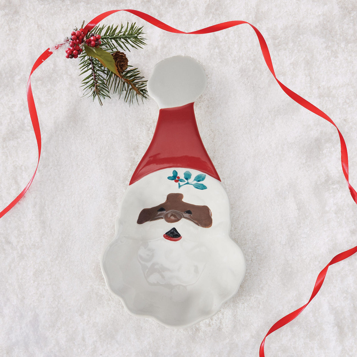 Snowman shaped Winterberry spoon rest shown with facial features and green leaf embellishment beside a red ribbon.