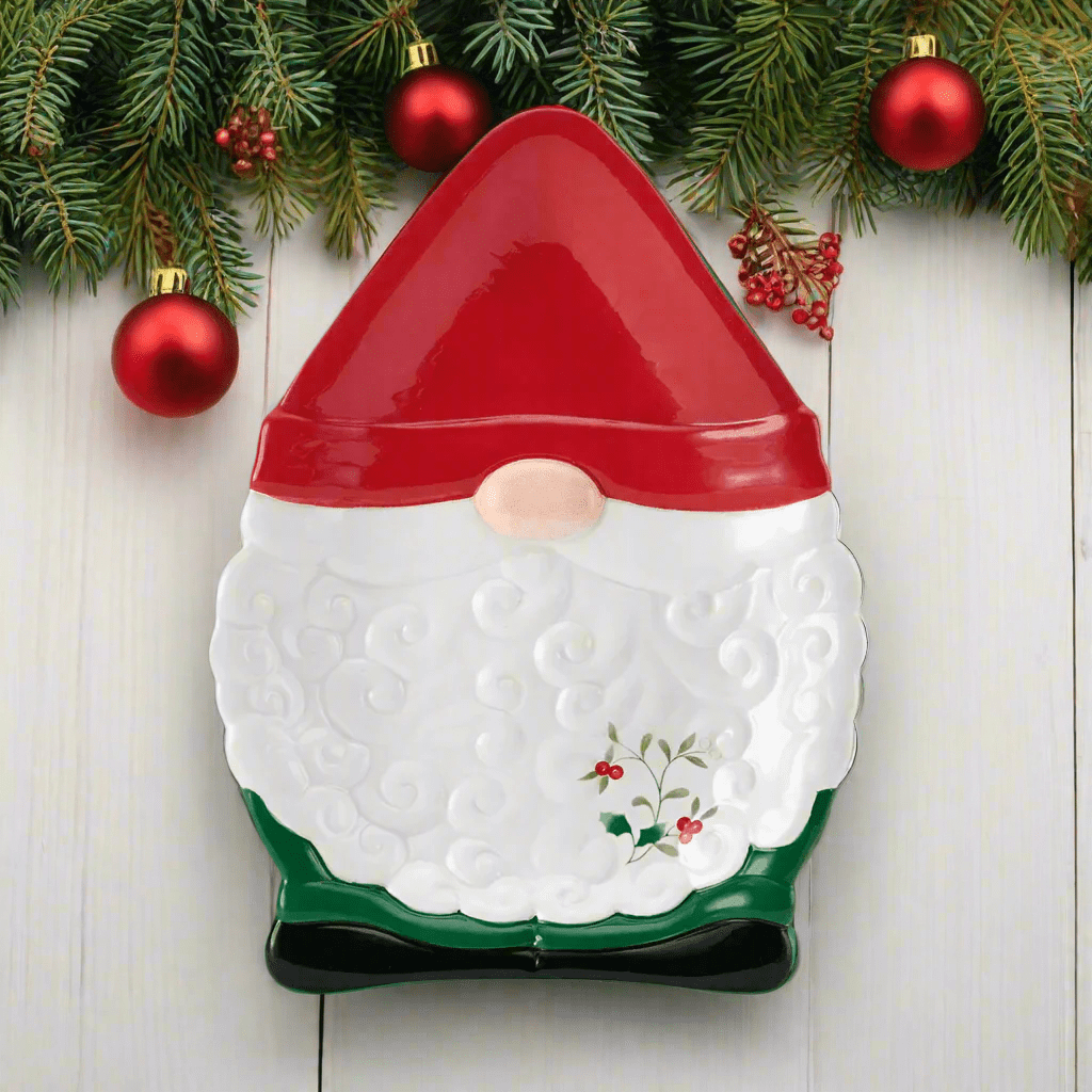 Winterberry Gnome Figural Cookie Plate in red white and green with holly accents shown on a wooden surface.