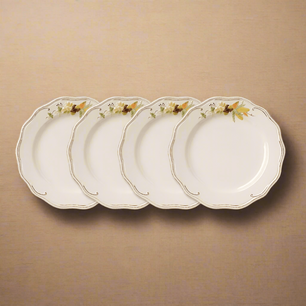 Four cream dinner plates with scalloped edges and floral border arranged in a row.