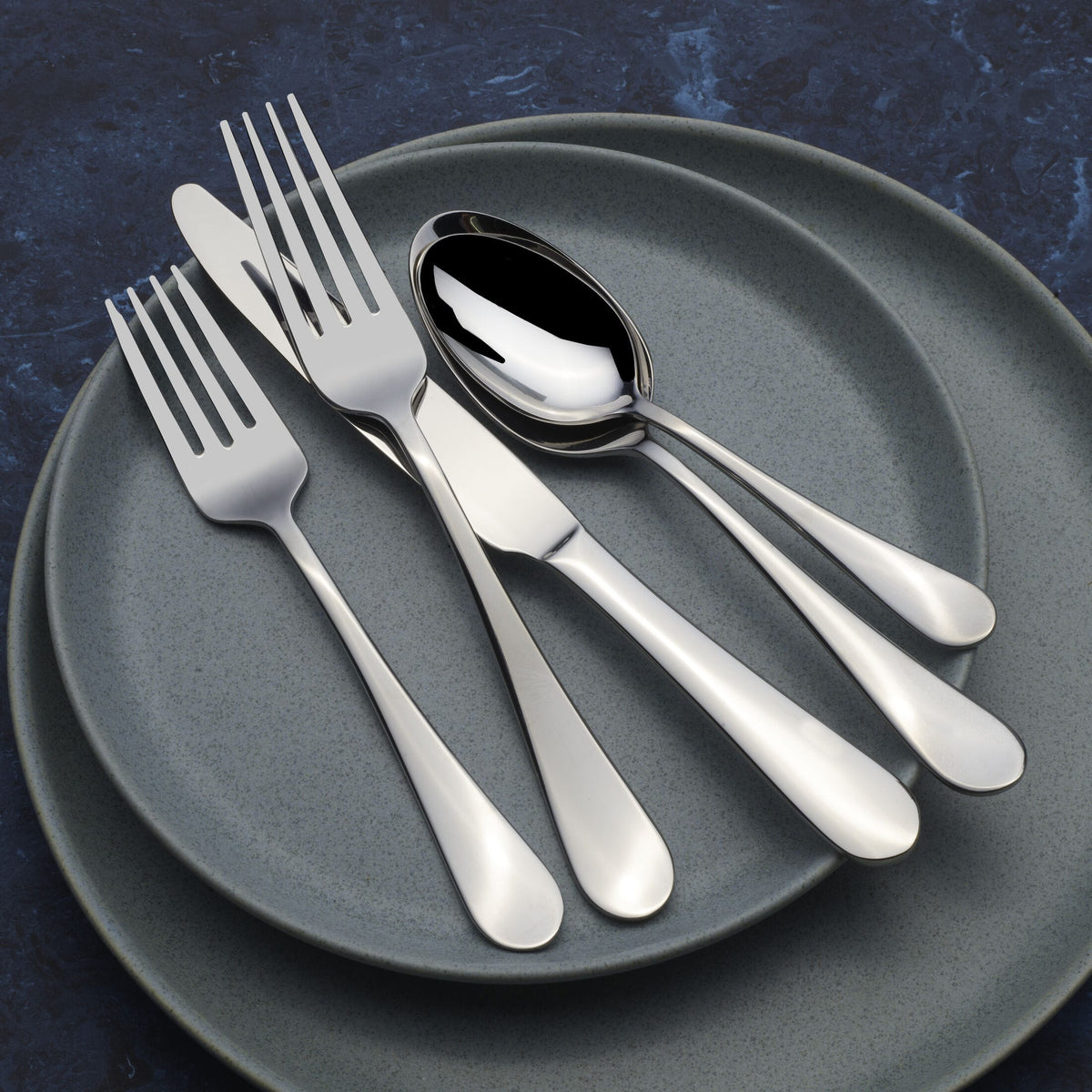 Forks knife and spoon arranged on a blue plate against a dark textured backdrop