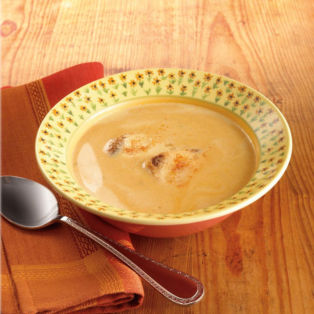 Pistoulet rim soup bowl with yellow floral rim filled with creamy soup on a wooden table with a napkin and spoon.