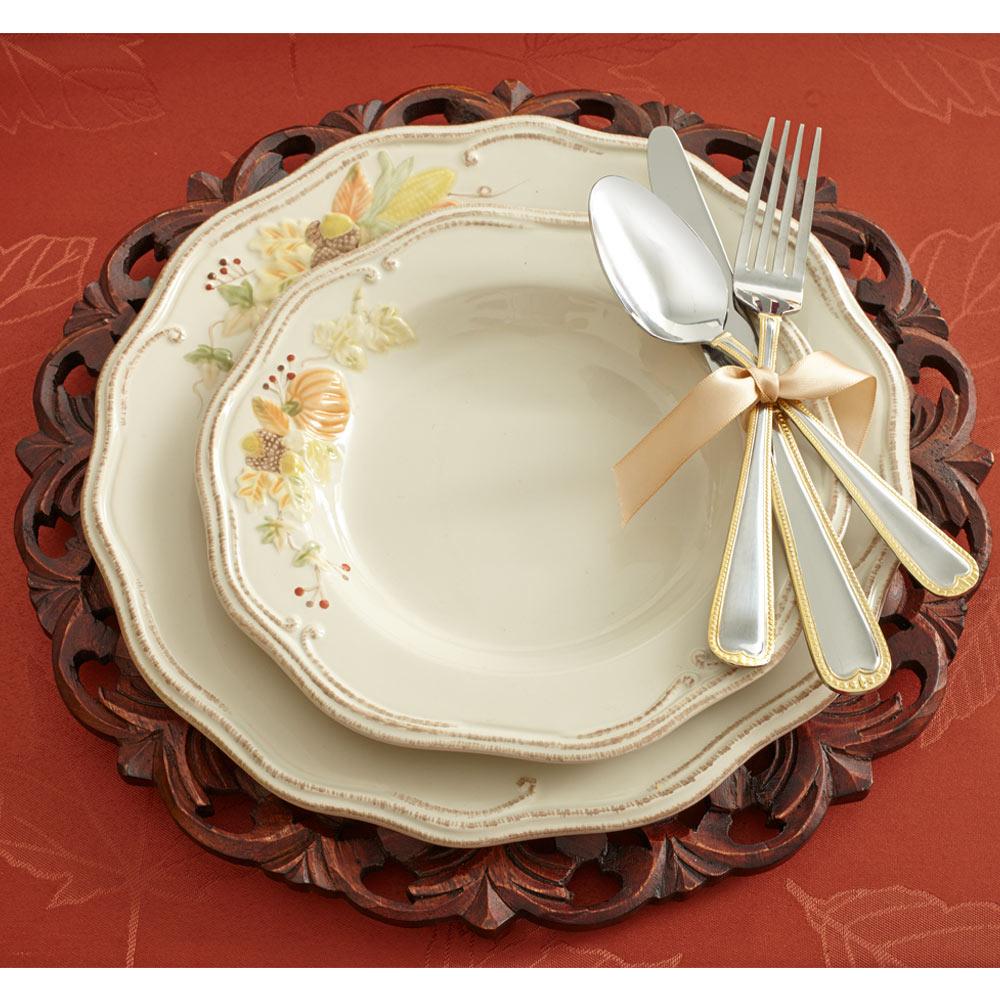 Place setting with Plymouth style plates and utensils tied with a pale ribbon on a red tablecloth.